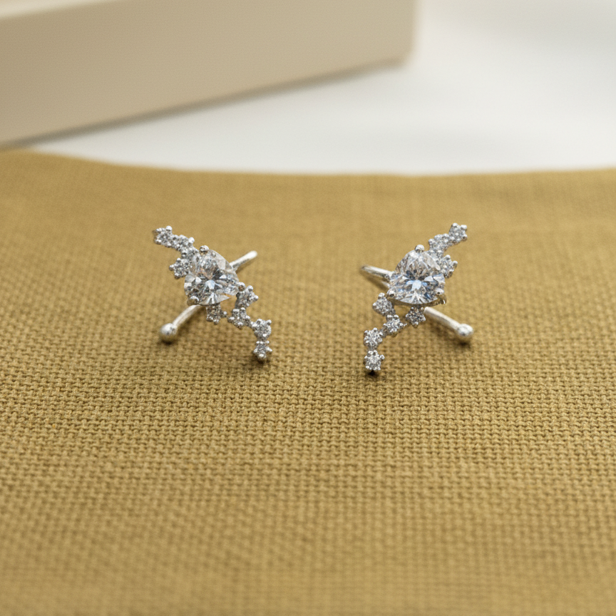 Pair of silver earrings with clear stones on a beige fabric background